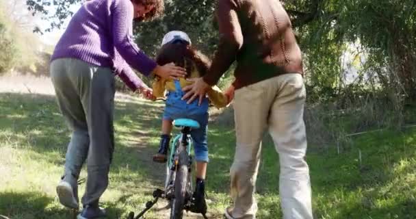 Padres ayudando a su hija a aprender a andar en bicicleta al aire libre — Vídeos de Stock
