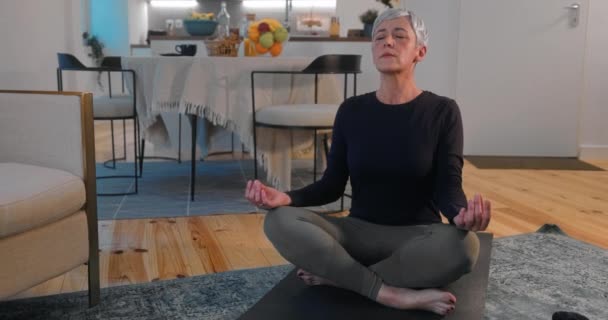 Mulher sênior praticando meditação de ioga em um tapete em casa — Vídeo de Stock