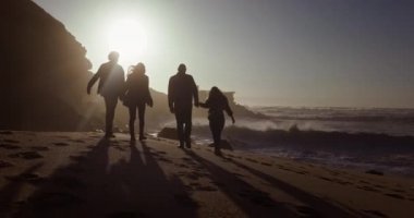 Bir grup arkadaş gün batımında sahilde yürüyor.