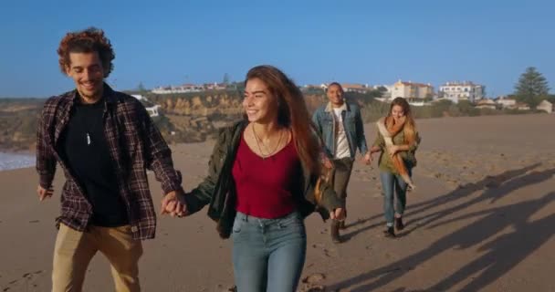 Twee koppels rennend aan het strand bij zonsondergang — Stockvideo