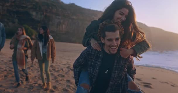 Young couple piggyback ride on the beach at sunset — Stock Video