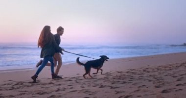 Gün batımında sahilde köpekle koşan genç bir çift.