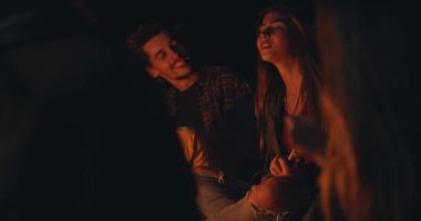 Sahildeki şenlik ateşinde gitar çalan genç bir kız.