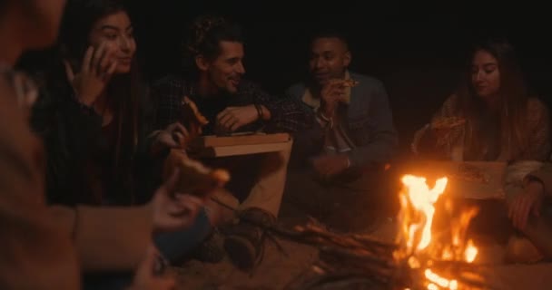 Grupo de amigos comendo pizza take-away na fogueira da praia — Vídeo de Stock