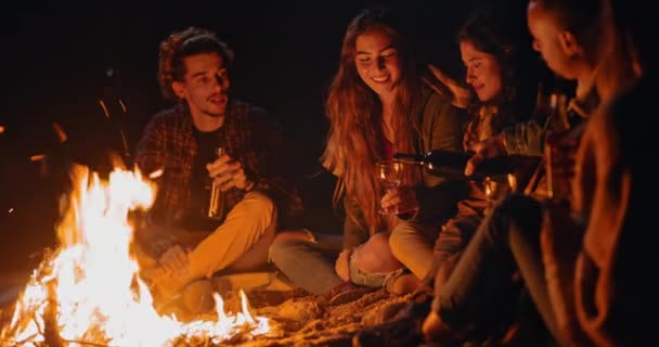 Přátelé pití nalévání víno láhev na pláži táborák v noci — Stock video