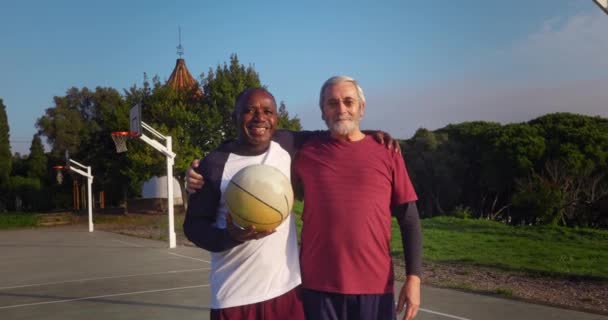 Двое старших мужчин обнимаются и проводят баскетбол на открытом воздухе — стоковое видео