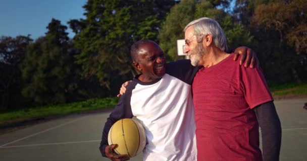 Afro-Amerikaanse senior man omarmen vriend houden basketbal op buitenshuis rechtbank — Stockvideo