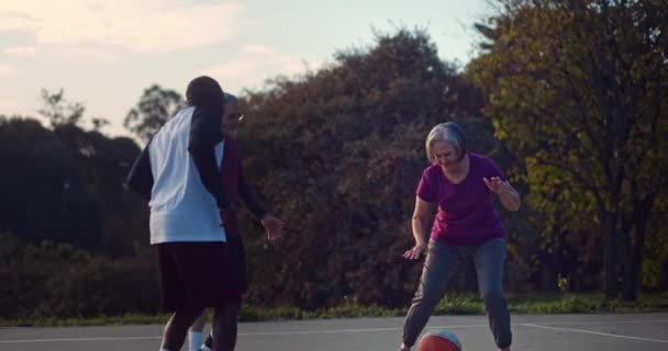 Старшая женщина дриблинг баскетбол с друзьями на открытом корте — стоковое видео