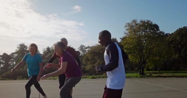 Femme âgée jouant au basketball avec un groupe de personnes âgées en plein air court — Video