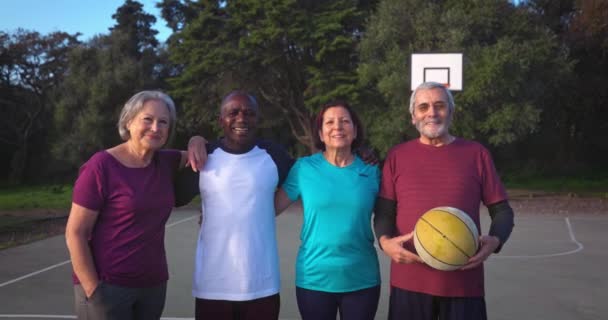 Grupo de personas mayores abrazando la celebración de baloncesto en la cancha al aire libre — Vídeos de Stock