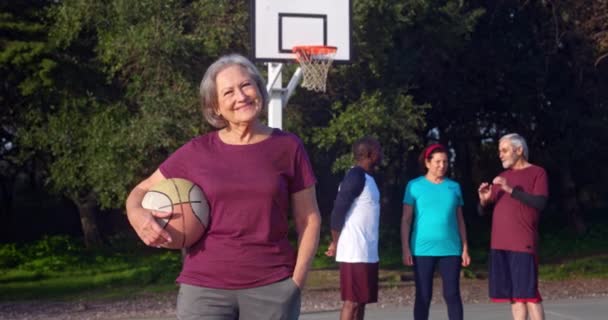 Femme âgée debout souriant avec basket sur le terrain extérieur — Video