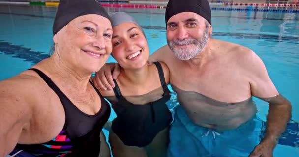 Grootouders met kleindochter nemen mobiele telefoon selfie in overdekt zwembad — Stockvideo
