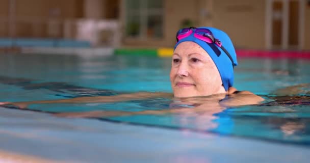 Mujer mayor sosteniendo junto a la piscina haciendo ejercicio en piscina cubierta — Vídeos de Stock