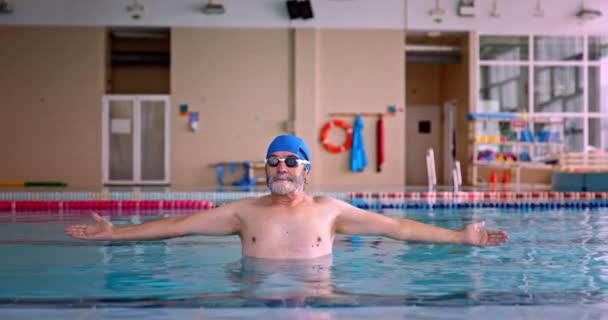 Hombre mayor estirando los brazos dentro de la piscina cubierta — Vídeos de Stock