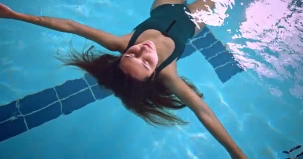 Mujer joven flotando en la piscina cubierta con pelo libre — Vídeos de Stock