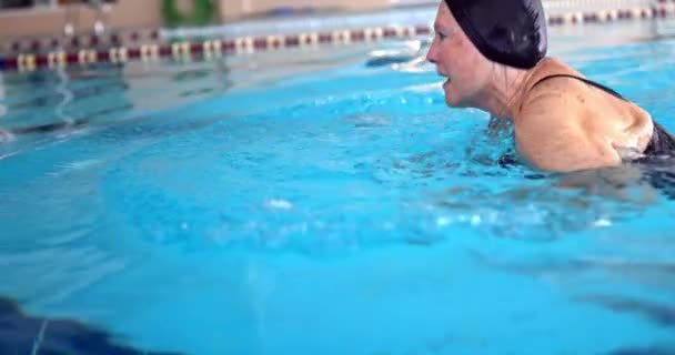 Mujer mayor nadando en piscina cubierta — Vídeo de stock