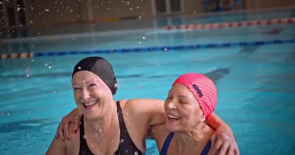 Las mujeres mayores saltando salpicaduras de agua que se divierten en la piscina cubierta — Vídeos de Stock