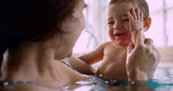 Baby skrattar leker med mamma röra ansiktet i inomhuspoolen — Stockvideo