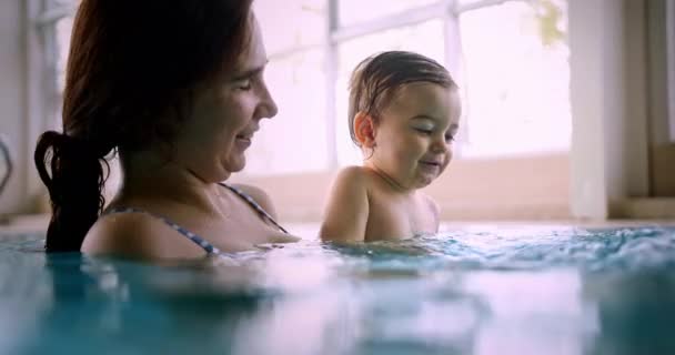 Mor och glad baby leende stänk vatten i inomhuspool — Stockvideo