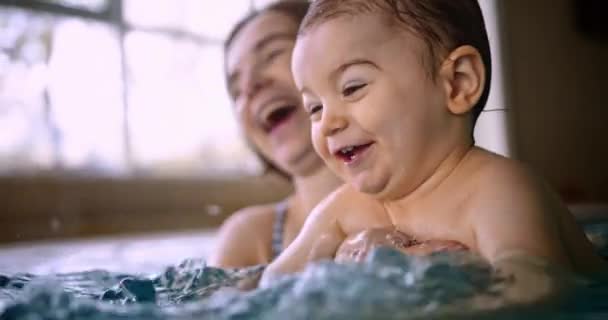 Happy baby splashing water playing with mom in indoor pool — Stock Video