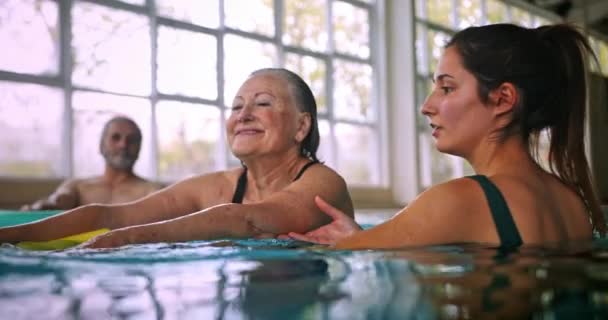 Instructor helping senior woman aerobics class with pool noodle Stock Footage