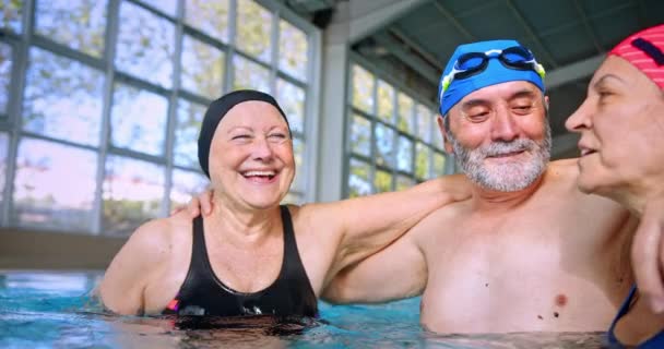 Felice gruppo di amici anziani sorridenti che si abbracciano nella piscina coperta — Video Stock