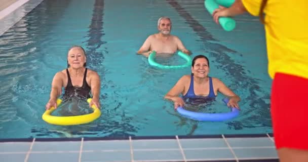 Entrenador dando clase de aeróbic senior de fideos de piscina en la piscina — Vídeo de stock