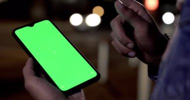 Geceleri dışarıda yeşil ekran cep telefonunu dinleyen bir adam var.