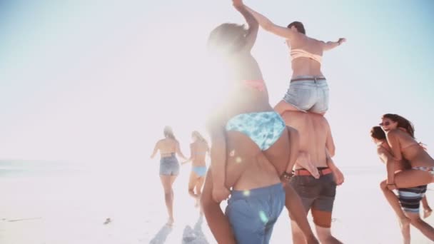 Amigos tendo corridas de piggyback em uma praia — Vídeo de Stock