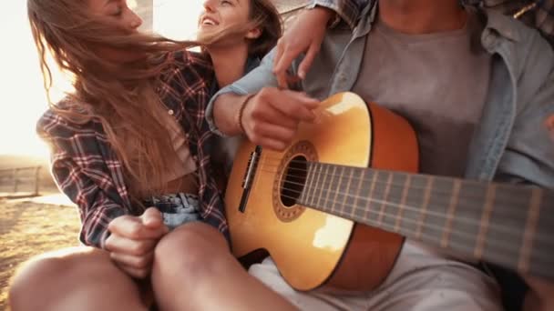 Adolescentes escuchando a un chico tocando su guitarra — Vídeo de stock