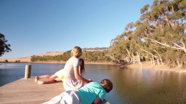 Sisters and brother sitting on a jetty — Stock Video