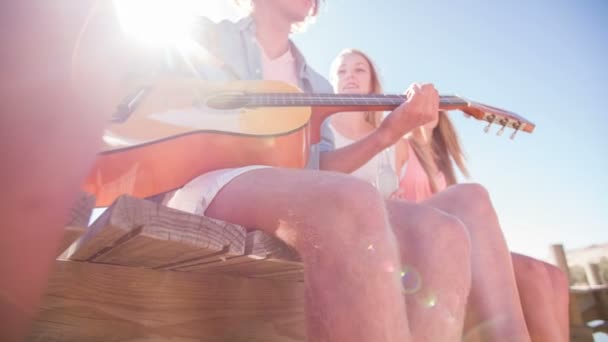 Mann spielt Gitarre für Freunde auf einem Steg — Stockvideo