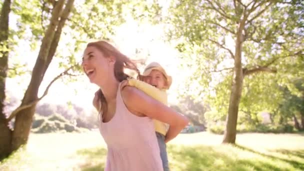 Mamá piggybacking su niño niña en parque — Vídeo de stock