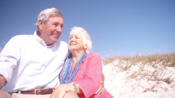 Retired couple sitting on sand at the beach — Stock Video