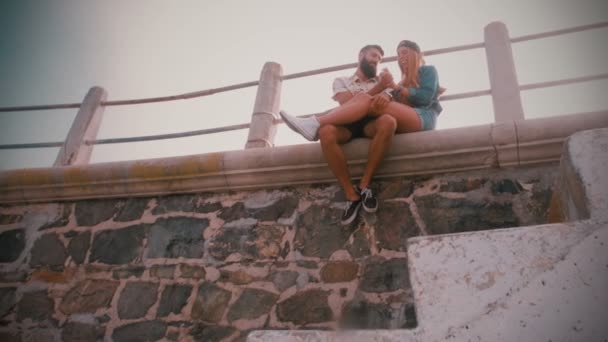 Hipster par sitter på en vägg tillsammans — Stockvideo