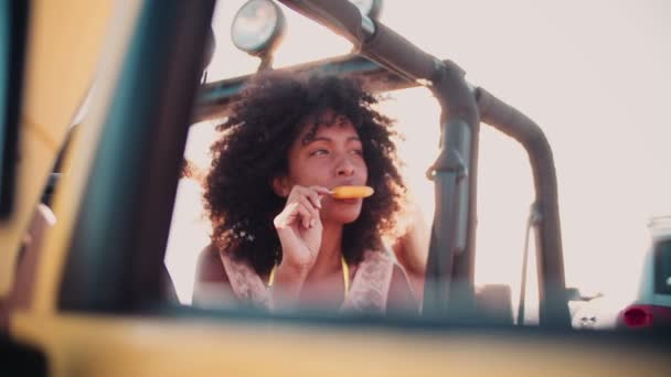 Chica africana comiendo paleta en el coche — Vídeos de Stock