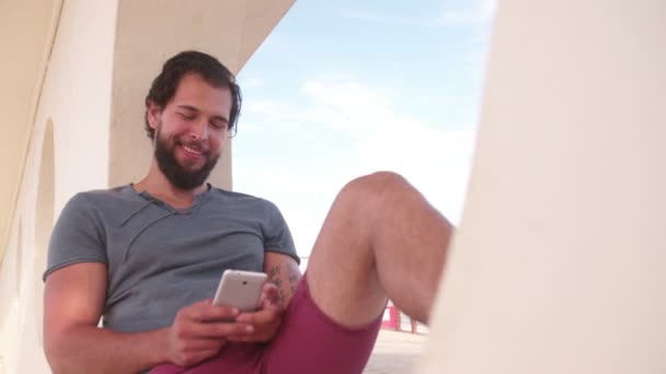 Kerl schaut auf Handy am Strand — Stockvideo