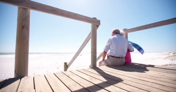 Пожилая пара, сидящая вместе на пляже — стоковое видео