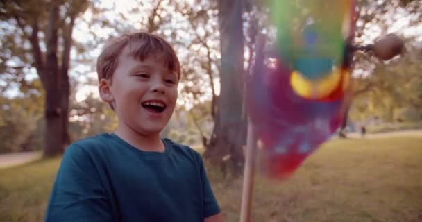 Menino olhando para um moinho de vento de brinquedo colorido — Vídeo de Stock