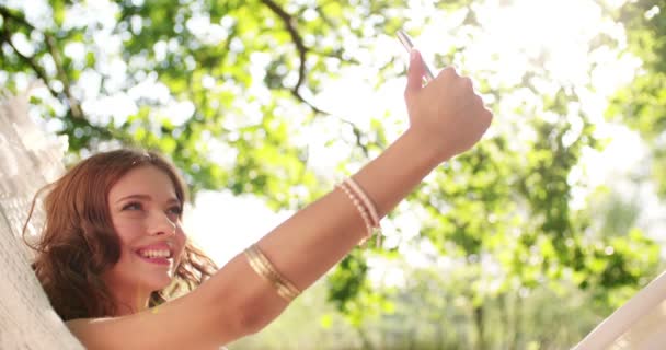 Mädchen macht ein Selfie in einer Hängematte im Park — Stockvideo