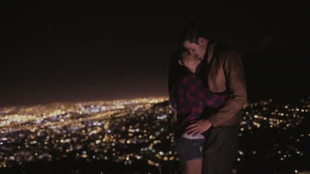 Pareja besándose con luces de la ciudad en el fondo — Vídeo de stock