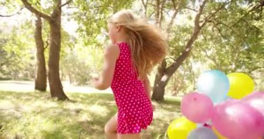 Mutlu bir şekilde balonları taşıyan neşeli küçük kız
