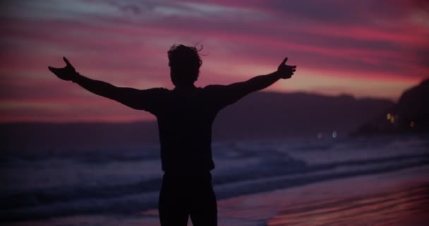 Хлопець висловлює свободу на пляжі на заході сонця — стокове відео