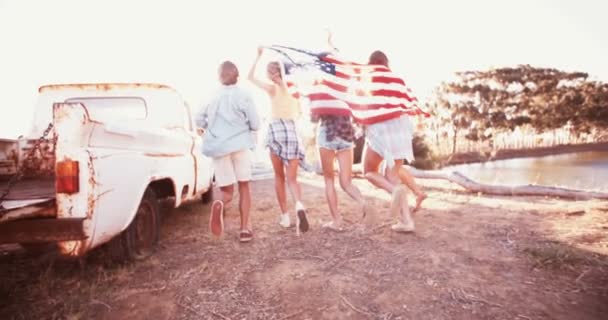 Adolescentes corriendo con una bandera americana en el resplandor solar — Vídeo de stock