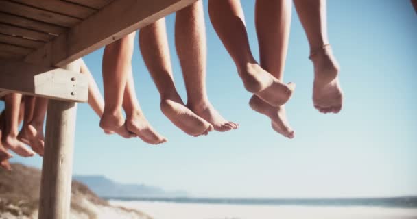 Beine von Freunden, die zusammen auf einer Strandpromenade sitzen — Stockvideo