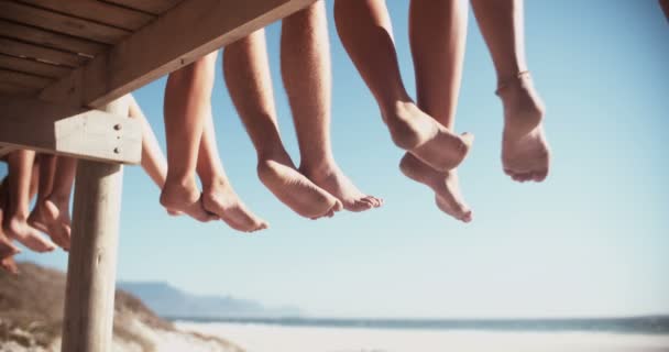 Legs of friends sitting on a beach boardwalk together — Stock Video