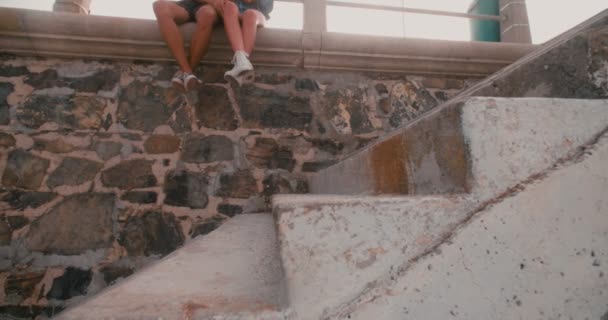 流行に敏感なカップルの足が石の壁の上に座って — ストック動画