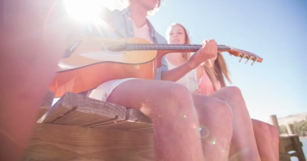 Mann spielt Gitarre für Freunde auf einem Steg im Freien — Stockvideo