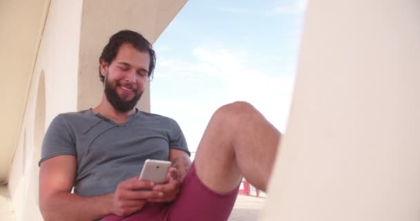 Un tipo mirando el teléfono en la playa — Vídeos de Stock
