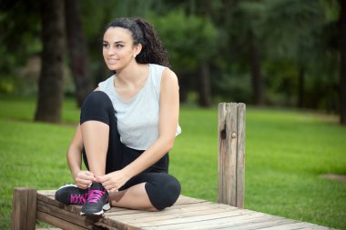 Siyah saçlı gülümseyen kadın üzerinde spor ayakkabı bağcıklarımı bağlama